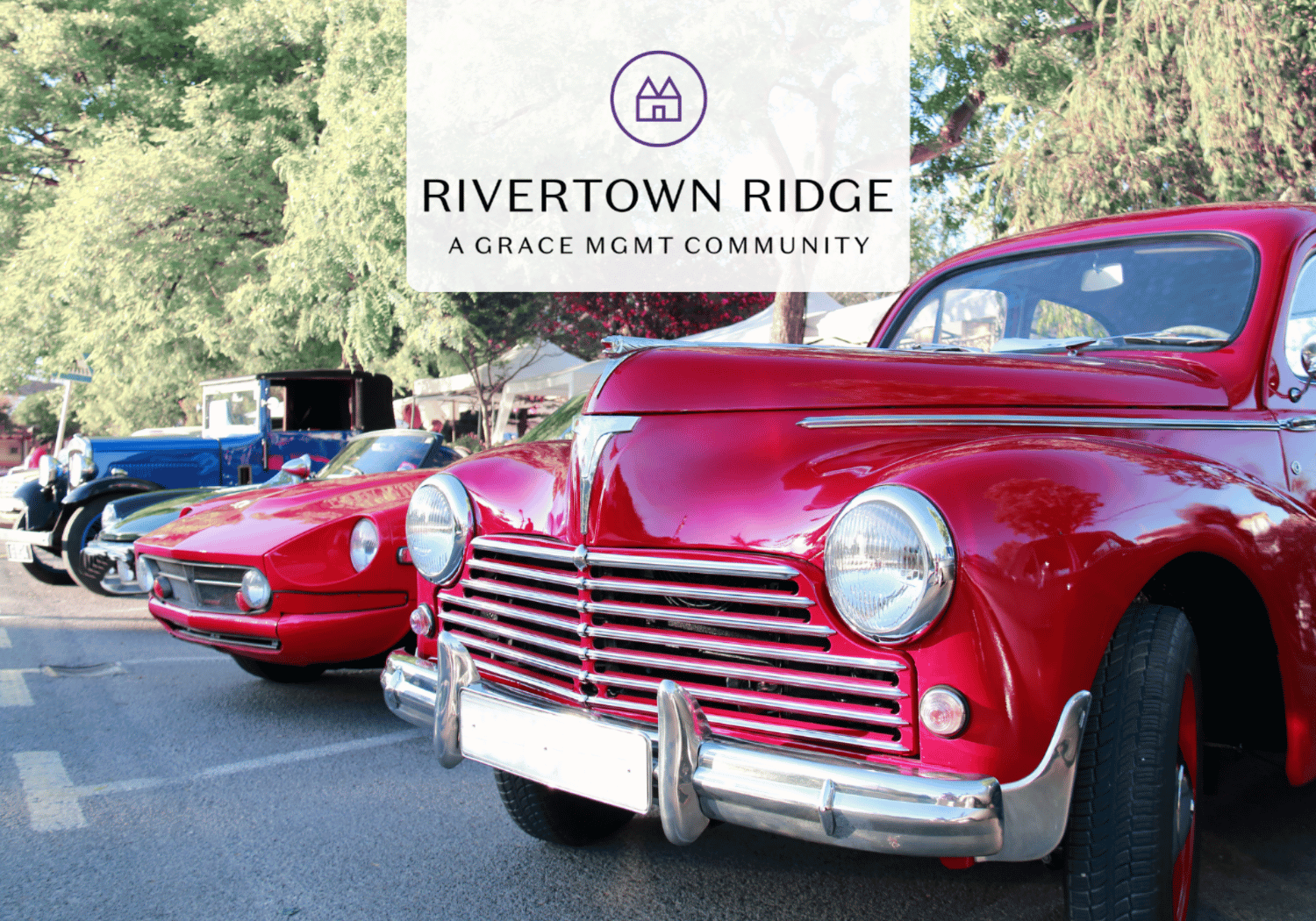 Vintage cars on display at Rivertown Ridge community event, with a prominent logo banner overhead.